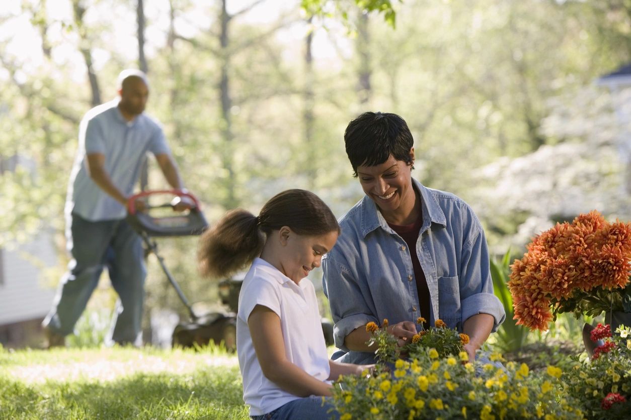 Family gardening together in a yard with flowers and lawn mower